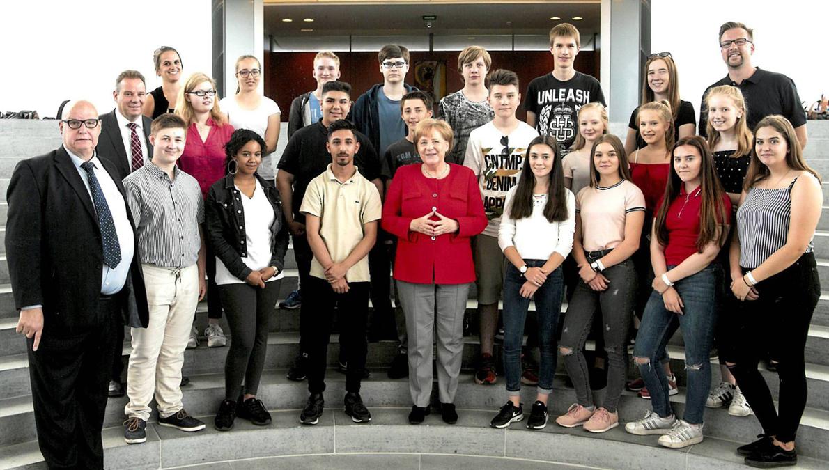 Von Schülern umringt steht Kanzlerin Angela Merkel (CDU) in der Mitte, links die Bundestagsabgeordneten Andreas Mattfeldt und Hans-Georg Lambertz. © bpb